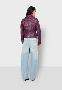 Fialová kožená bunda s dobře padnoucím střihem, bez zdobení, v kombinaci se světle modrými kalhotami s širokými nohavicemi. Hladká textura a strukturovaný tvar.