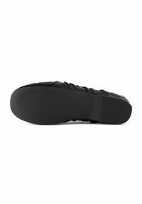 Semelle de chaussure noire avec une surface en caoutchouc texturée pour une meilleure adhérence. Présente une surface lisse et des bords arrondis, affichant un design simple et minimaliste.