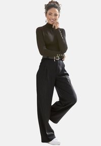 Schwarzes Langarmoberteil mit Knopfdetails, kombiniert mit hochtaillierten gestreiften Hosen und weißen Sneakern. Minimalistisches, elegantes Design.