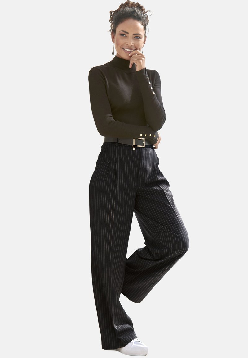 Schwarzes Langarmoberteil mit Knopfdetails, kombiniert mit hochtaillierten gestreiften Hosen und weißen Sneakern. Minimalistisches, elegantes Design.