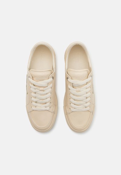 Sneakers in pelle beige con accenti texturizzati, punta tonda e lacci bianchi. Presentano un branding minimale sul lato e sulla linguetta.