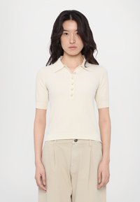 Short-sleeve, cream-colored polo shirt made of textured fabric, featuring a button-up collar and five buttons down the front.