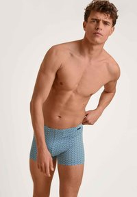 Blauwe zwemboxers met een geometrisch ontwerp, gemaakt van een soepel materiaal, met een snit tot halverwege de bovenbenen en een elastische tailleband.