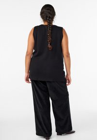 Črni zgornji del brez rokavov in široke črne hlače iz mehkega materiala z gladko teksturo, sproščenim krojem in stranskimi razporki na zgornjem delu.