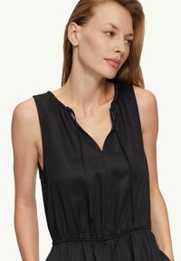 Vestido negro sin mangas con escote fruncido, parte delantera en forma de V, detalle de cordón y cintura elástica, hecho de una tela ligera.