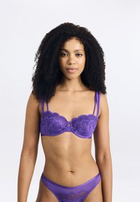 Conjunto de lingerie roxa em renda, com um sutiã com aro e padrões florais e alças ajustáveis, combinado com uma cueca transparente a condizer.