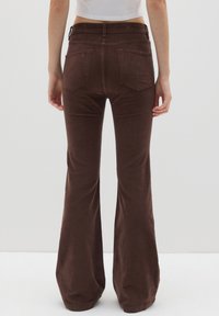 Bruine fluwelen uitlopende broek met een middelhoge taille, vaste achterzakken en een zachte, gestructureerde oppervlakte.