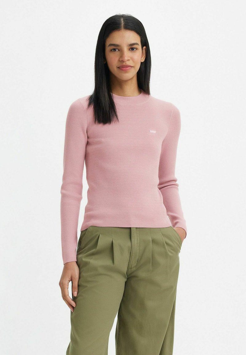 Maglia rosa a maniche lunghe con scollo rotondo e dettaglio del logo sul petto, abbinata a pantaloni larghi verde oliva.