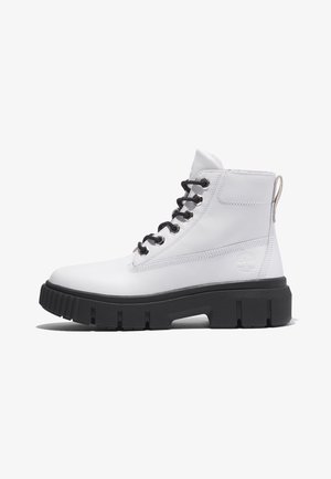 Bottes de cheville en cuir blanc avec lacets noirs, semelle épaisse noire, coutures contrastantes et une languette au talon arborant un logo.