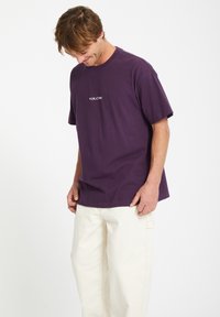 Lilla bomulds T-shirt med rund hals og korte ærmer, med "VOLCOM" logo trykt i hvid på brystet.