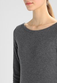 Graues Langarmshirt mit Rundhals, aus weichem Stoff gefertigt. Eine Nahaufnahme hebt die glatte Textur und das taillierte Design hervor.