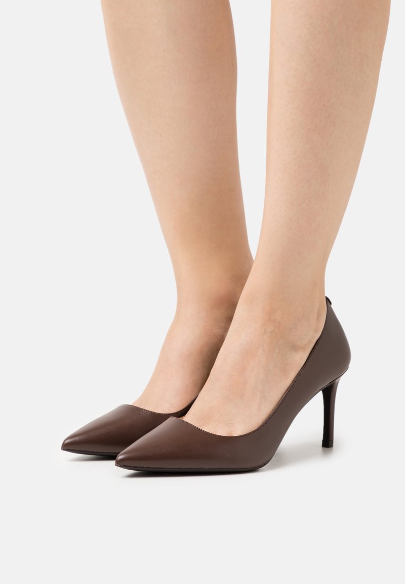 Smeđe kožne cipele s visokom potpeticom, s oštrim vrhom, glatkom teksturom i elegantnim siluetom; minimalistički dizajn bez vidljivih metalnih detalja.