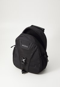 Mochila negra de nylon con un acabado texturizado. Presenta una forma curva, correa ajustable, bolsillos laterales de malla y cierre de hebilla.