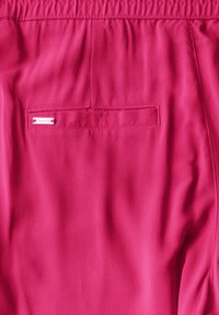 Rosa tygshorts med elastisk midja, en bakficka med etikett och en slät, lätt textur.