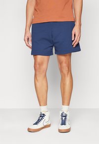 Shorts bleu marine avec taille élastique, fabriqués en tissu doux. Associés à des baskets montantes blanches avec des accents bleu marine et une semelle texturée.