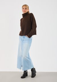 Rjava rebrasta pletena turtleneck pulover, svetlo modri široki jeans z raztrganim robom in črne gležnjarje z zaponkami.