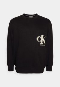 Svart sweatshirt i bomullsblandning, rundad hals, långa ärmar, med vit "ck"-logotyp och textdetalj på vänster bröstområde.