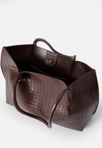 Bolso tote de cuero marrón con un diseño texturizado de tejido, asas suaves y un cierre de botón magnético. La parte superior abierta revela el espacio interior.