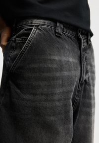 Jean noir en denim présentant un effet délavé avec des nuances variées, conception traditionnelle à cinq poches et passants pour ceinture, vu de côté.