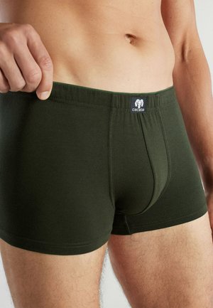 Man wearing dark green boxer briefs, holding waistband to show fit, visible torso and upper legs, brand logo centered on waistband.