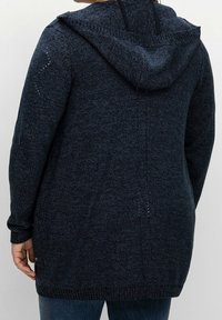 Ciemnoniebieski sweter zapinany na guziki z kapturem, z wzorzystym materiałem, bocznymi kieszeniami i ściągaczami przy mankietach. Wydłużony tył o luźnym kroju.