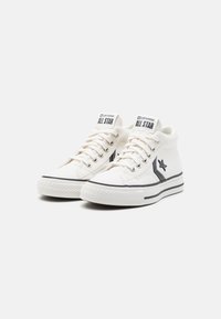 Białe półwysokie trampki Converse All Star z czarnym logo gwiazdy, czarnym paskiem na podeszwie i białymi sznurowadłami na gładkim tle.