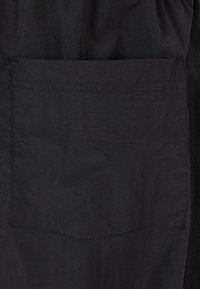 Zwarte stof met een matte textuur bevat een rechthoekige zak. De naaddetails zijn subtiel en mengen zich met het materiaal.