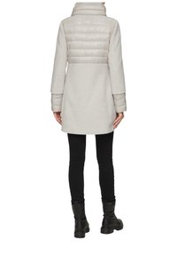 Hellgrauer Mantel mit einem gesteppten oberen Abschnitt, gerader Schnitt und langen Ärmeln. Strukturmaterial mit hohem Kragen. Trägt man über schwarzen Hosen und Stiefeln.