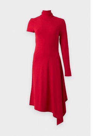 Femme debout portant une robe asymétrique rouge avec une manche courte et une manche longue, assortie à des sandales à talons hauts à brides foncées.