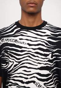 Fekete-fehér póló zebrasáv mintával, puha anyagból készült, fekete bordázott nyakkal és nyomtatott szöveges részlettel.