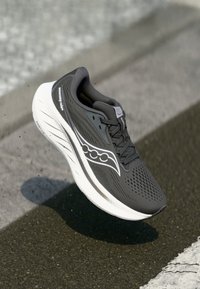 Chaussure de course noire avec tige en mesh, accents blancs et semelle rembourrée. Présente un design épuré et une surface texturée pour l'adhérence.