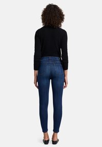 Jeans skinny bleus avec une taille haute, fabriqués en denim, dotés de poches arrière, d'une texture lisse et d'une silhouette ajustée.