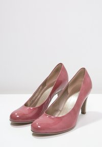 Escarpins en cuir verni rose avec un bout arrondi, un talon en bois mince et une texture lisse et brillante. Les accents comprennent une semelle intérieure métallique.