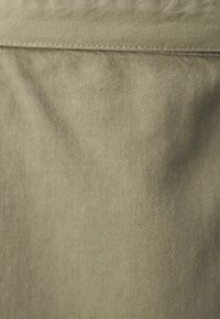 Béžová bavlněná látka s jemnou rypsovou strukturou. Materiál je hladký s mírným leskem a rovnoměrně prošitými švy podél okrajů.