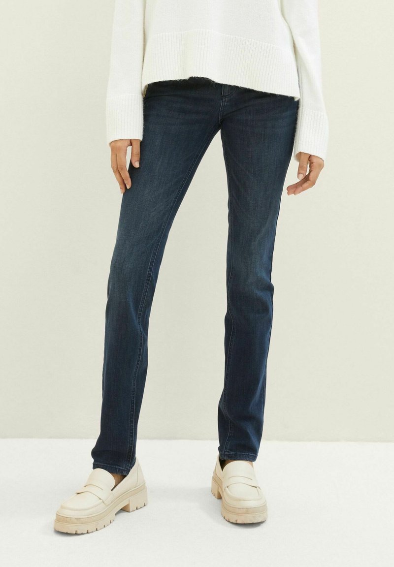 Sötétkék, slim-fit szabású farmernadrág, denim anyagból készült, krém színű platform mokaszinokkal párosítva. A pulóver fehér, bordázott mandzsettákkal.
