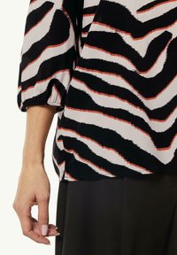 Mehrfarbige Bluse mit einem schwarzen, weißen und orangefarbenen Zebramuster. Strukturierter Stoff mit drei Viertelärmeln und elastischen Bündchen.