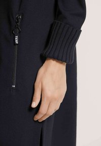 Schwarzes Reißverschlusskleid mit gestreiftem Bündchendetail, das einen glatten Stoff und einen Seitenschlitz zeigt. Verfügt über einen Reißverschlussanhänger mit Markenbeschriftung.