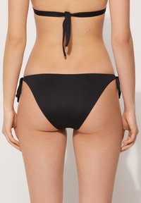 Czarne majtki bikini z gładkiego materiału, o umiarkowanym pokryciu, z regulowanymi wiązaniami po bokach, co pozwala na indywidualne dopasowanie.