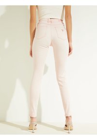 Svetle růžové pruhované skinny džíny s vysokým pasem, zadními kapsami a kontrastním švem, doplněné béžovými botami na podpatku s otevřenou špičkou.