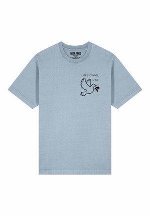 T-shirt di cotone azzurro chiaro con una grafica nera di una colomba che tiene un ramo d'ulivo con la scritta "LIBRE COMME L’AIR" sopra. Maniche corte.