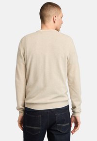 Beige svetr vyrobený z měkkého materiálu, s kulatým výstřihem, dlouhými rukávy a žebrovanými manžetami. Jednoduchý, bezproblémový design bez výrazných detailů.