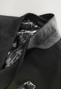Chaqueta negra a medida con cuello de fieltro gris y forro estampado floral en tonos de negro y gris. Textura suave y diseño estructurado.