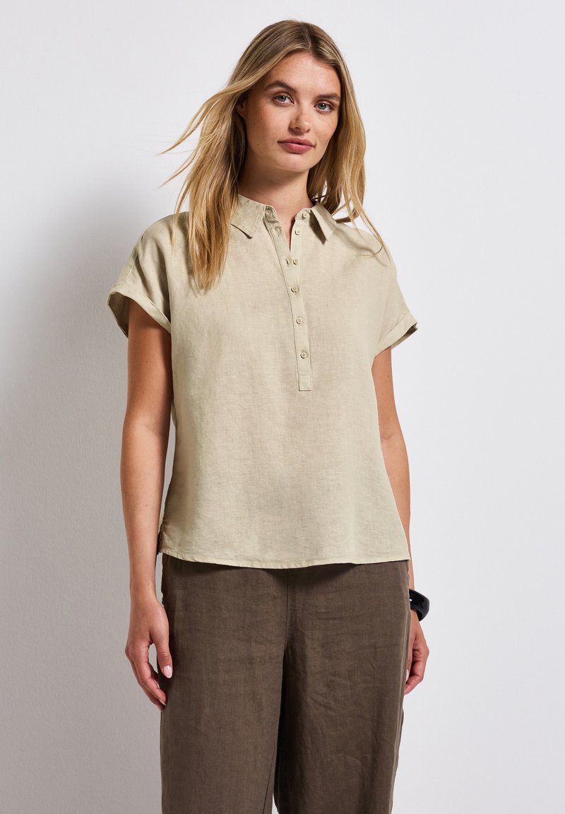 Camicetta a maniche corte con colletto in lino beige chiaro, con una chiusura a bottoni, abbinata a pantaloni larghi in lino marrone. Tessuto morbido, vestibilità comoda.