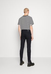Camiseta a rayas negras combinada con pantalones oscuros. La camiseta tiene mangas cortas y un corte relajado. Los pantalones son ajustados con una textura suave. Botas negras completan el look.