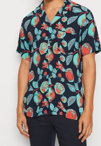 Lyhythihainen, napillinen paita, jonka kankaan väri on tummansininen ja jossa on kirkkaanvärisiä hedelmä- ja kukkakuoseja punaisessa ja turkoosissa, sileä materiaali, rento istuvuus.