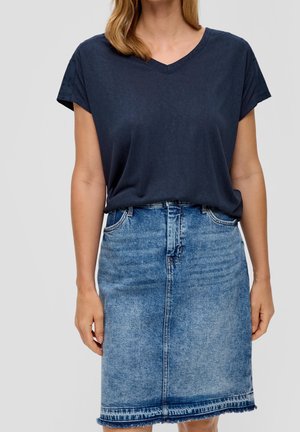 Kvinde iført en marineblå V-hals kortærmet top, stoppet ned i et falmet blåt denim knælængde skjørt med frynset kant.