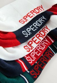 Meerkleurige katoenen sokken gestapeld, met het "SUPERDRY" logo in contrasterende draad. Kleuren zijn wit, rood, marineblauw en groen.