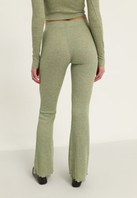 Ensemble en tricot côtelé vert composé d'un haut ajusté à manches longues et d'un pantalon évasé avec des bords effilochés, fabriqué à partir d'un tissu doux avec des éclats multicolores.