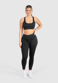 Set di reggiseno sportivo e leggings neri realizzati in tessuto elasticizzato con una texture liscia. Presenta un design aderente e una branding minima. Inclusa un paio di sneakers bianche.
