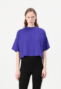 T-shirt corto viola con collo alto e maniche corte. Presenta un dettaglio logo discreto vicino al collo, realizzato in un tessuto morbido.